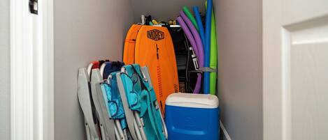 A narrow hallway with a white door on the left, a blue cooler, and various items including a blue and orange bag, a white and blue chair, and colorful foam rollers.