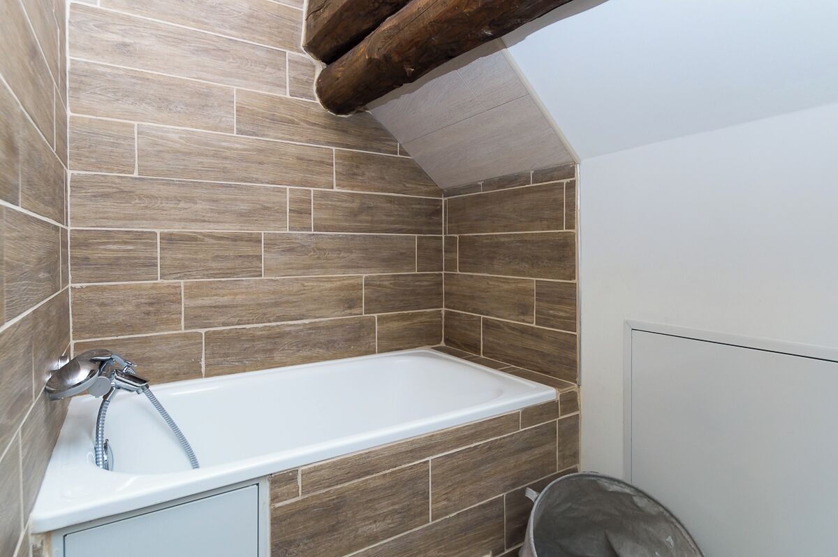 Un baño con bañera, azulejos de madera y un cabezal de ducha.