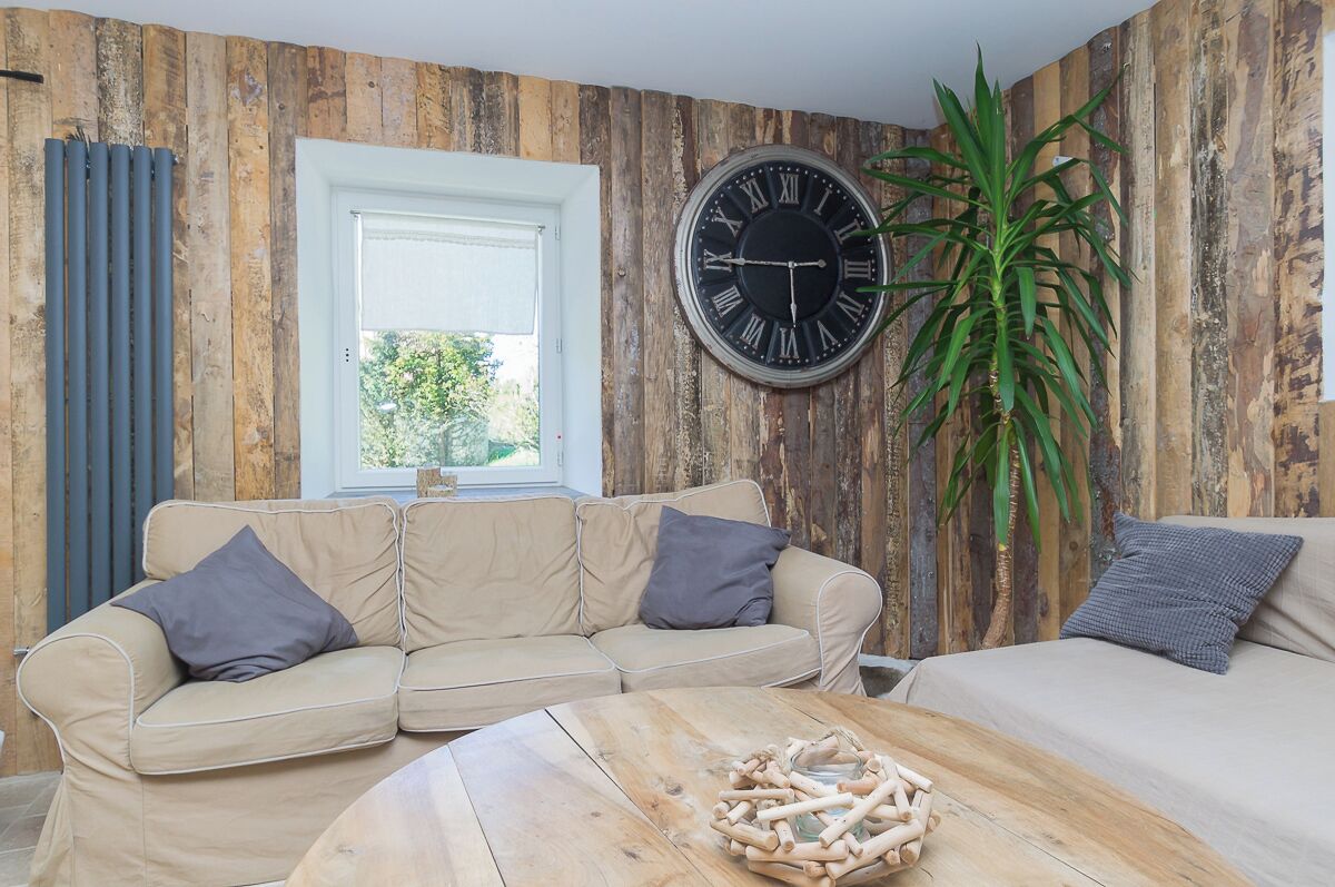 A room with a wooden wall, a large round clock, a beige sofa, a wooden coffee table, and a potted plant.