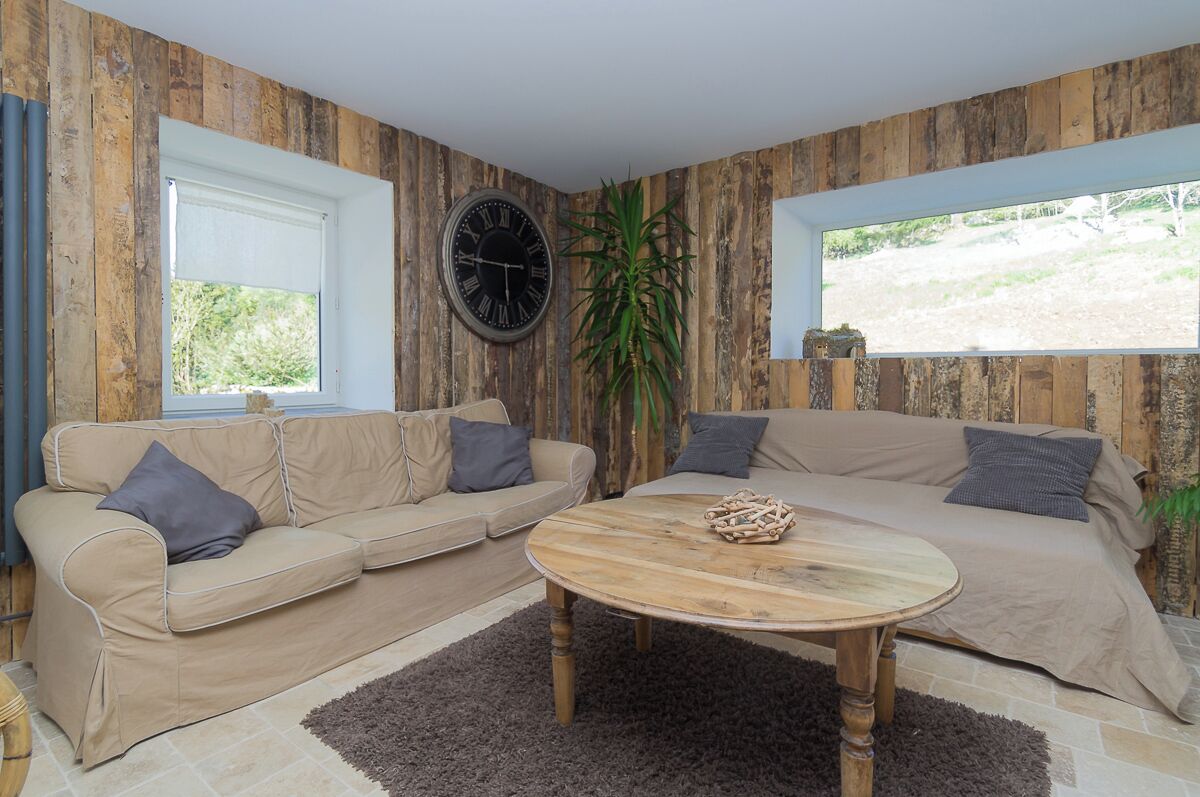 Ein Wohnzimmer mit zwei Sofas, einem Holztisch, einer Wanduhr und einem großen Fenster.