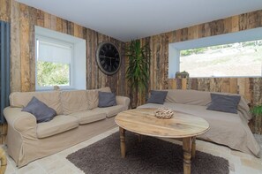 A living room with two sofas, a wooden coffee table, a wall clock, and a large window. - La Grange aux Fées - AUTRANS-MEAUDRE IN VERCORS (AUTRANS-MEAUDRE EN VERCORS)