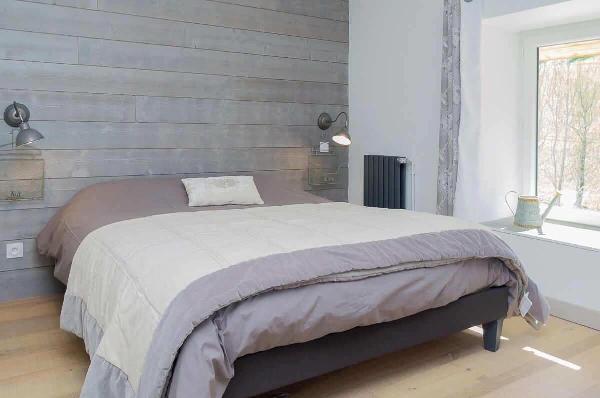 Ein Schlafzimmer mit einem Bett, Holzvertäfelung, zwei Wandlampen, einer Heizung und einem Fenster mit Blick.