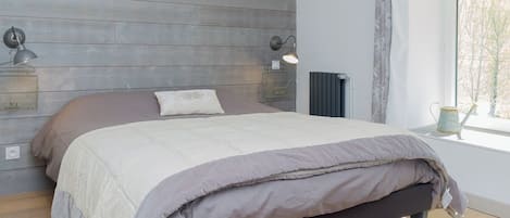 Ein Schlafzimmer mit einem Bett, Holzvertäfelung, zwei Wandlampen, einer Heizung und einem Fenster mit Blick.
