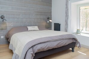 Quarto com cama, painéis de parede em madeira, duas luminárias e uma janela com vista, além de um radiador.