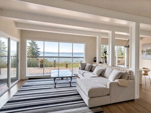 A spacious living room with a large sliding glass door leading to a deck, a sofa, a coffee table, and a view of the outdoors. - Delightful Studio apartment with AC in Seattle (Seattle)