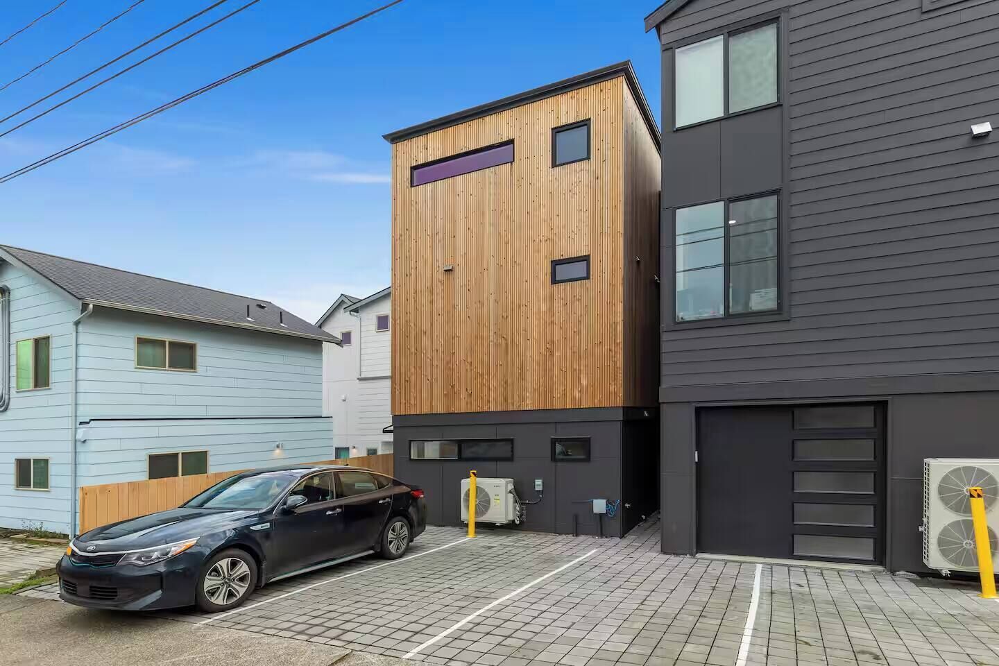 Een modern gebouw met een houten gevel en een donker uiterlijk, met een auto ervoor geparkeerd en een heldere lucht.