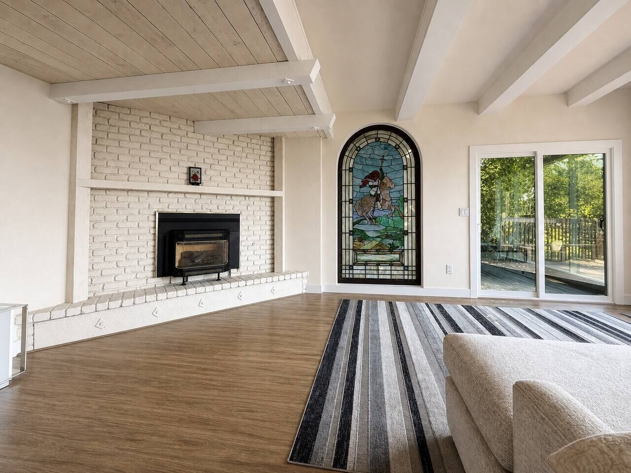 A spacious living room with a fireplace, a large window with a stained glass design, and a view of the outdoors.