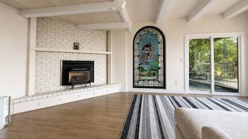 A spacious living room with a fireplace, a large window with a stained glass design, and a view of the outdoors.