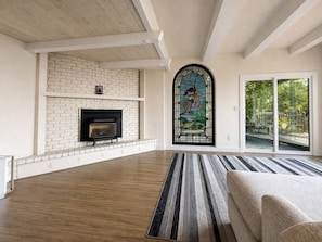 A spacious living room with a fireplace, a large window with a stained glass design, and a view of the outdoors.