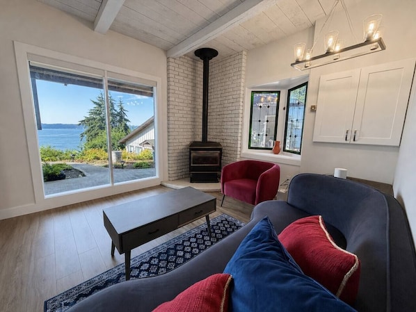 A living room with a fireplace, a sofa, a red chair, and a view of the outdoors.