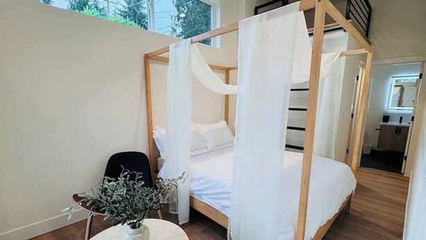 A bedroom with a four-poster bed, a round table with a plant, and a view of the outside through a window. - Delightful Studio apartment with AC in Seattle (Seattle)