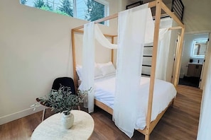 A bedroom with a four-poster bed, a round table with a plant, and a view of the outside through a window.