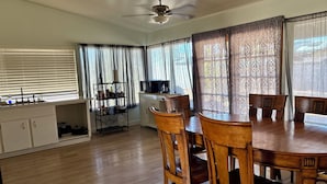 Uma sala de jantar com mesa e cadeiras de madeira, cozinha com pia e armários, e um ventilador de teto.