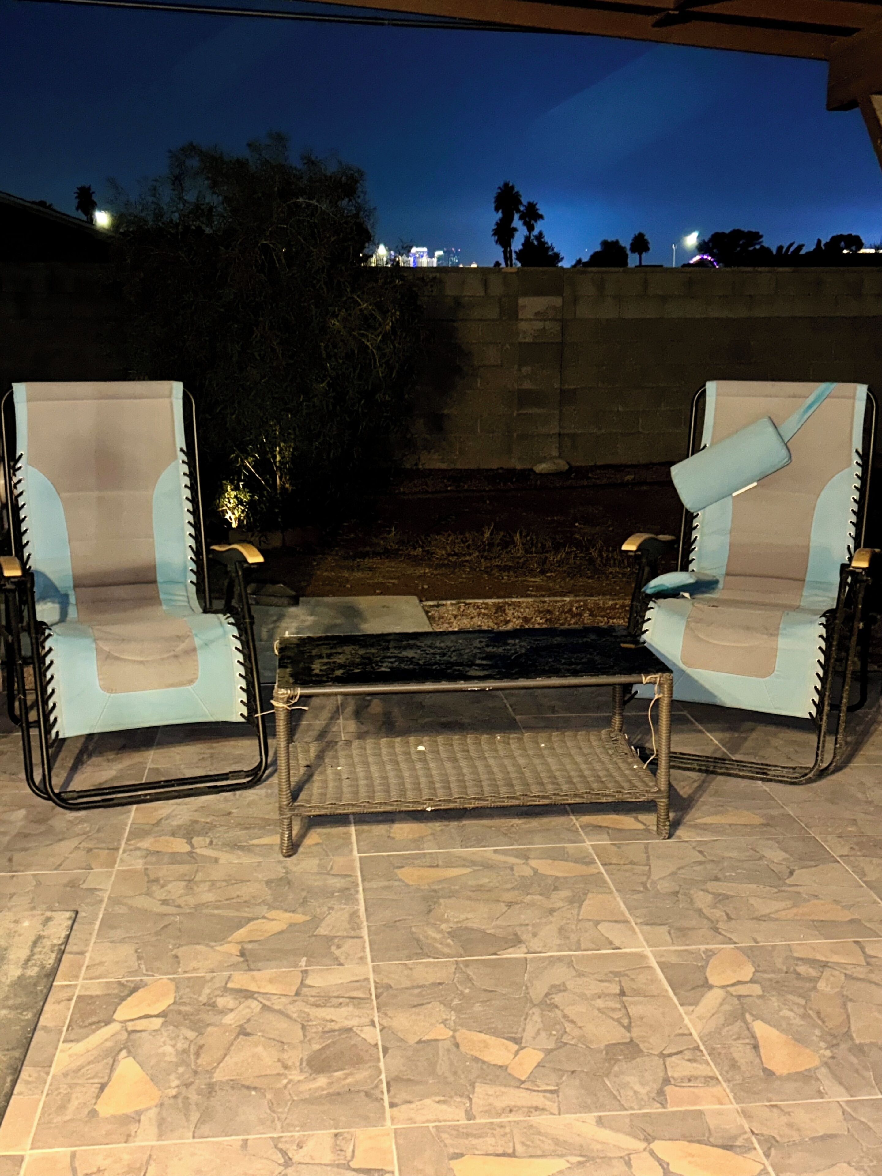 Two lounge chairs with cushions, a small table, and a stone-tiled patio area.