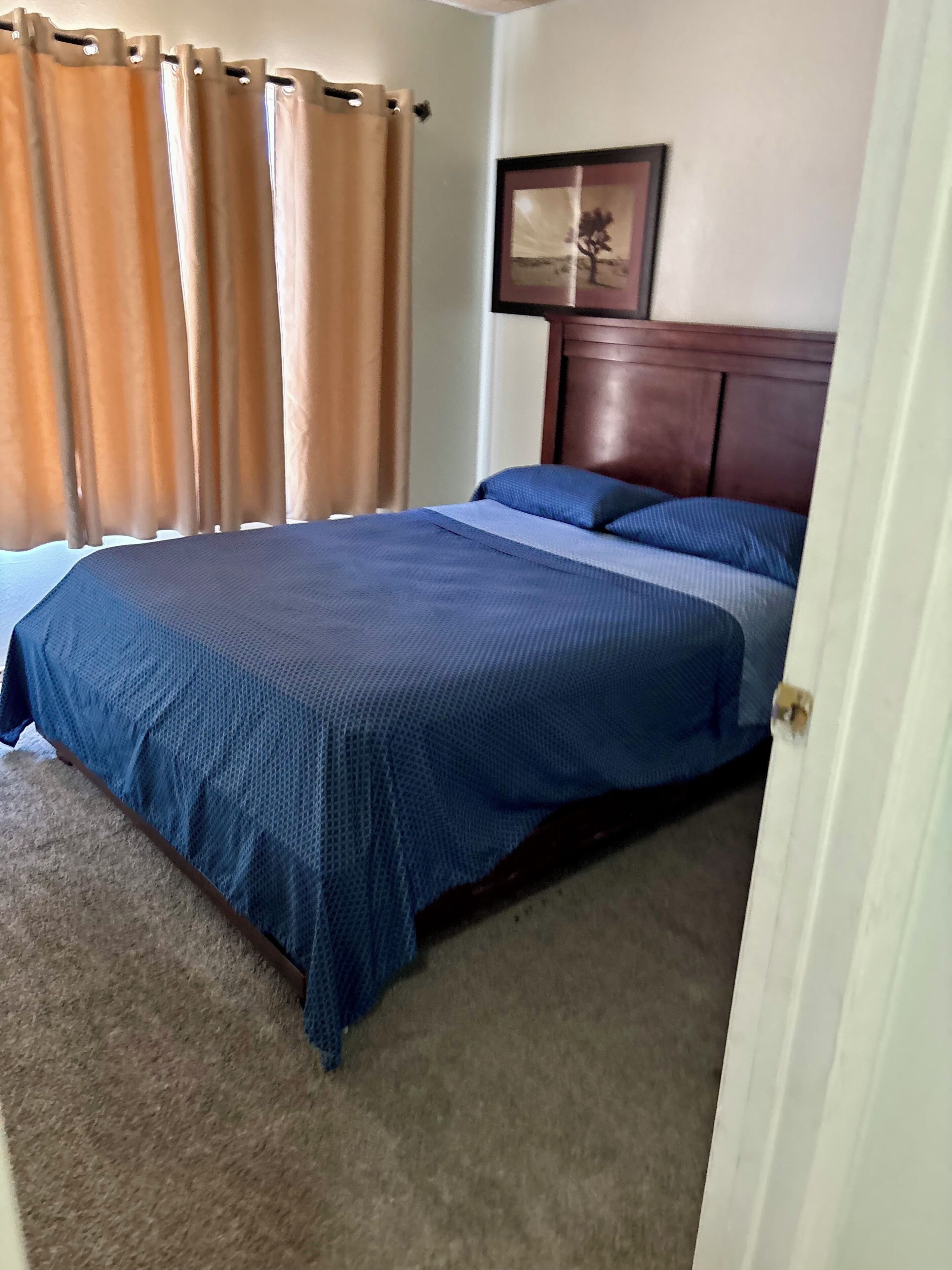 Une chambre à coucher avec un lit, une tête de lit, une fenêtre avec des rideaux et un tableau encadré au mur.