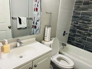 A bathroom with a white sink, toilet, and bathtub. There is a towel rack with a white towel and a shower curtain with a floral pattern.