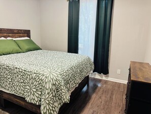 Een slaapkamer met een bed, een houten hoofdbord, een dressoir en een raam met gordijnen.