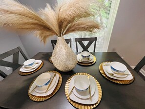 Una mesa de comedor dispuesta con platos, tazones y cubiertos, rodeada de sillas.