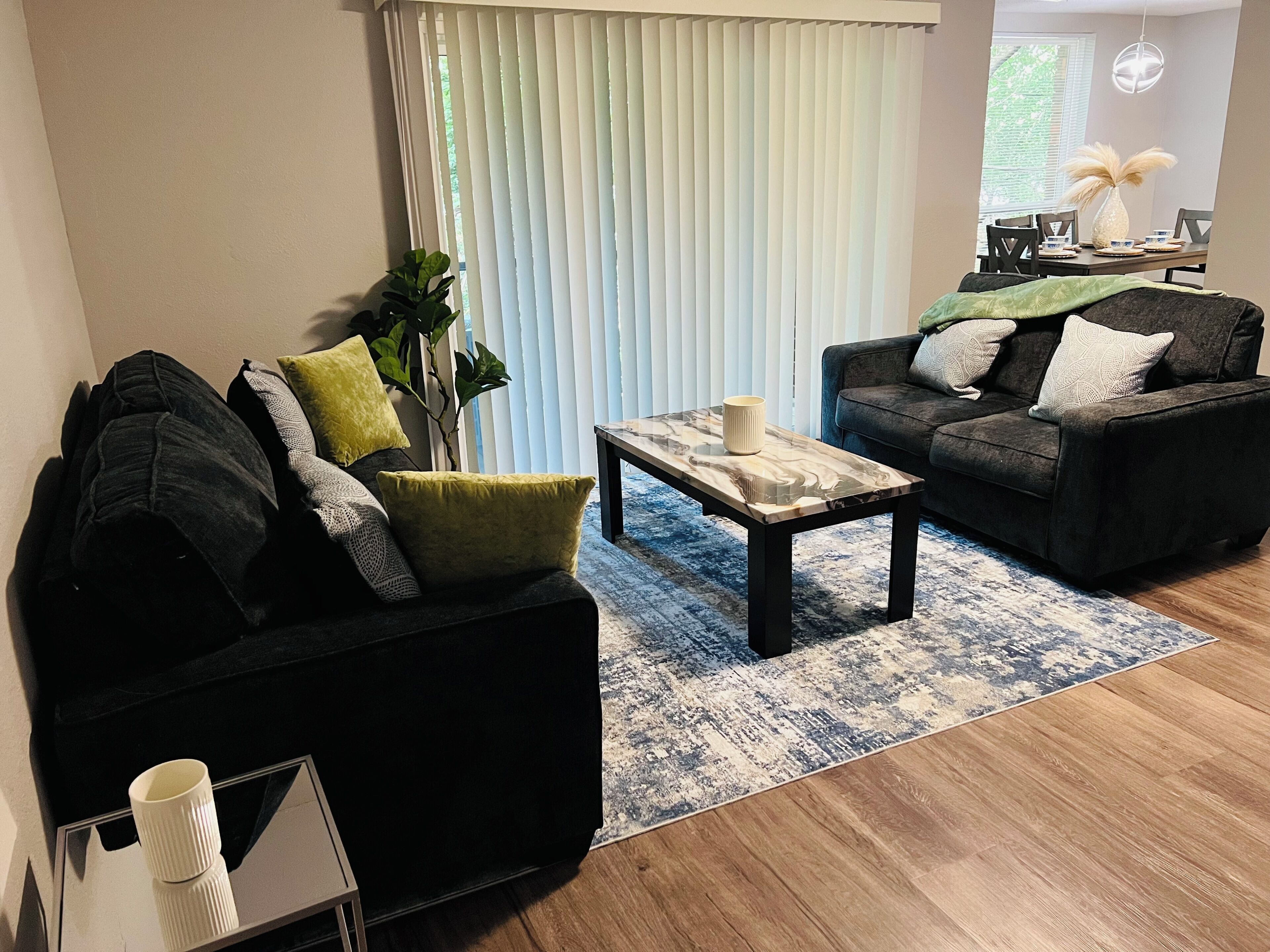 A modern living room with a black sofa, a coffee table, and a dining area with a table set for two.