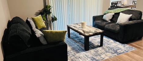 A modern living room with a black sofa, a coffee table, and a dining area with a table set for two.