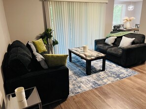 Una sala de estar moderna con un sofá negro, una mesa de centro y un comedor con una mesa dispuesta para dos personas.