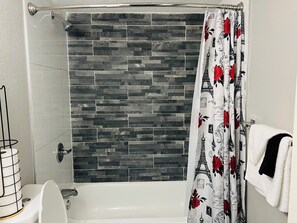 Un baño con cortina de ducha estampada con motivos florales, una bañera blanca y un perchero con una toalla blanca.