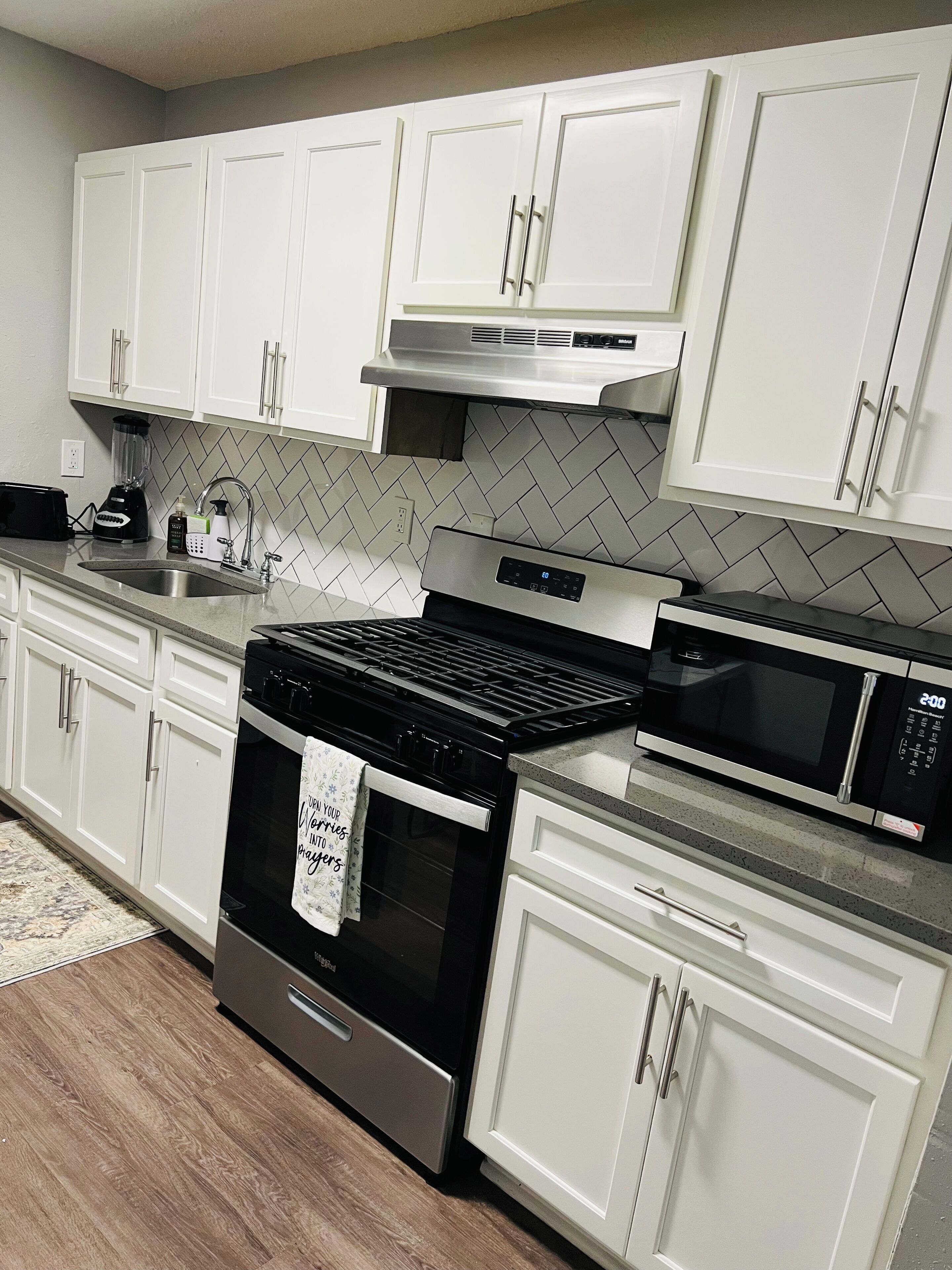 A modern kitchen with white cabinets, stainless steel appliances, and a herringbone tile backsplash.