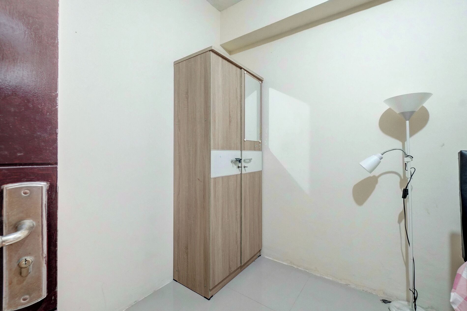 Una habitación con un armario de madera, una pared blanca y una lámpara de pie.
