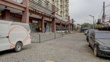 Un área pavimentada con una furgoneta estacionada a la izquierda, un edificio de varios pisos al fondo y un automóvil a la derecha.