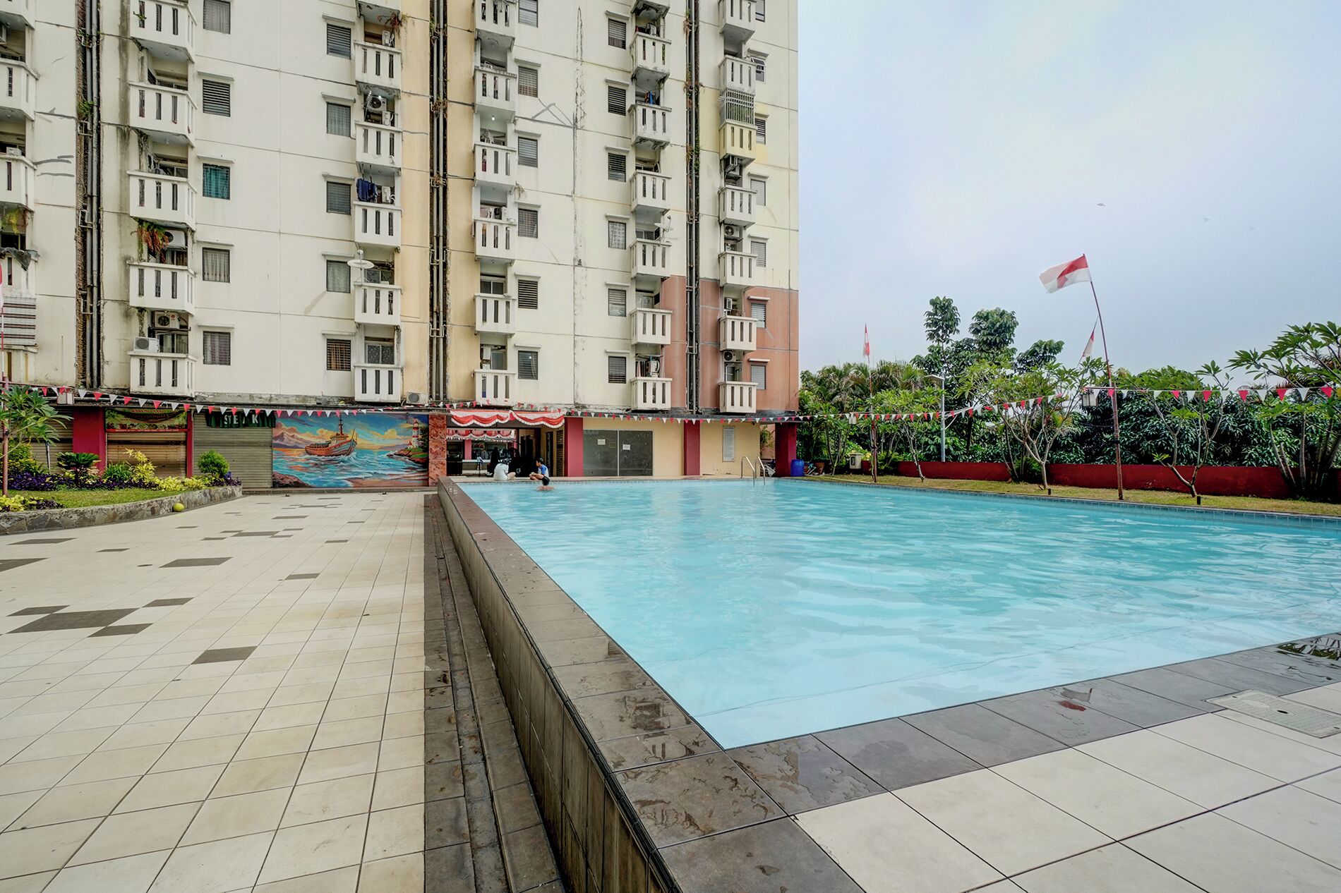 Zona de piscina con suelo de baldosas, un mural y una bandera.