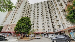 A high-rise residential building with multiple balconies, a central courtyard, and surrounding commercial establishments. - Apartemen Cibubur Village KaisarProperty (Kota Depok)
