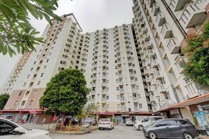 A high-rise residential building with multiple balconies, a central courtyard, and surrounding commercial establishments. - Apartemen Cibubur Village KaisarProperty (Kota Depok)