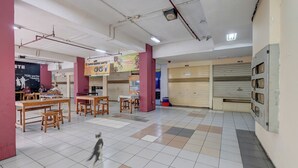 A spacious indoor area with tiled flooring, wooden tables, and chairs, and a dog walking through. - Apartemen Cibubur Village KaisarProperty (Kota Depok)