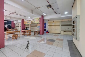 A spacious indoor area with tiled flooring, wooden tables, and chairs, and a dog walking through. - Apartemen Cibubur Village KaisarProperty (Kota Depok)