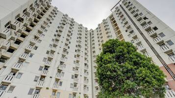 A high-rise residential building with multiple balconies and a large tree in front.