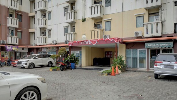 A multi-story building with a ground-level entrance, a covered waiting area, and a storefront. - Apartemen Cibubur Village KaisarProperty (Kota Depok)