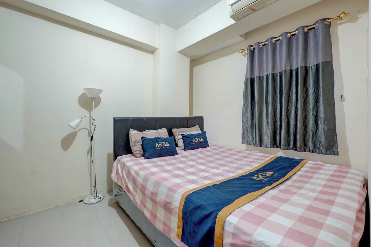 A hotel room with a bed, a floor lamp, and a window with curtains.
