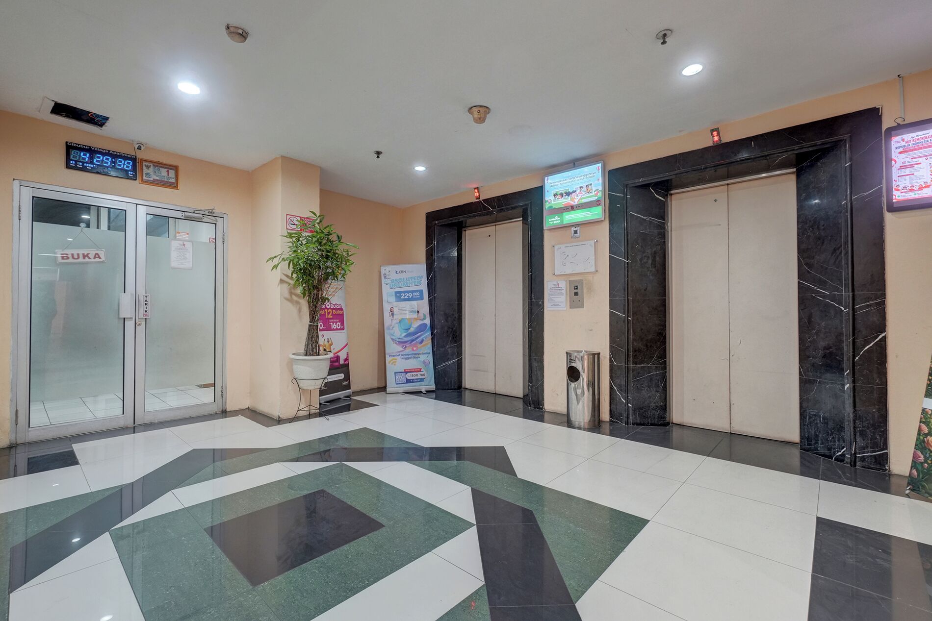 Um saguão com relógio digital, balcão de recepção, planta em vaso e piso de mármore.
