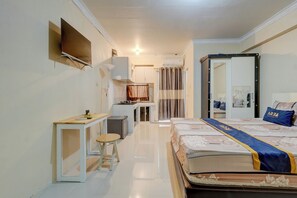 A hotel room with a bed, a small table, a chair, a TV mounted on the wall, and a bathroom visible through an open door. - Apartemen Cibubur Village KaisarProperty (Kota Depok)