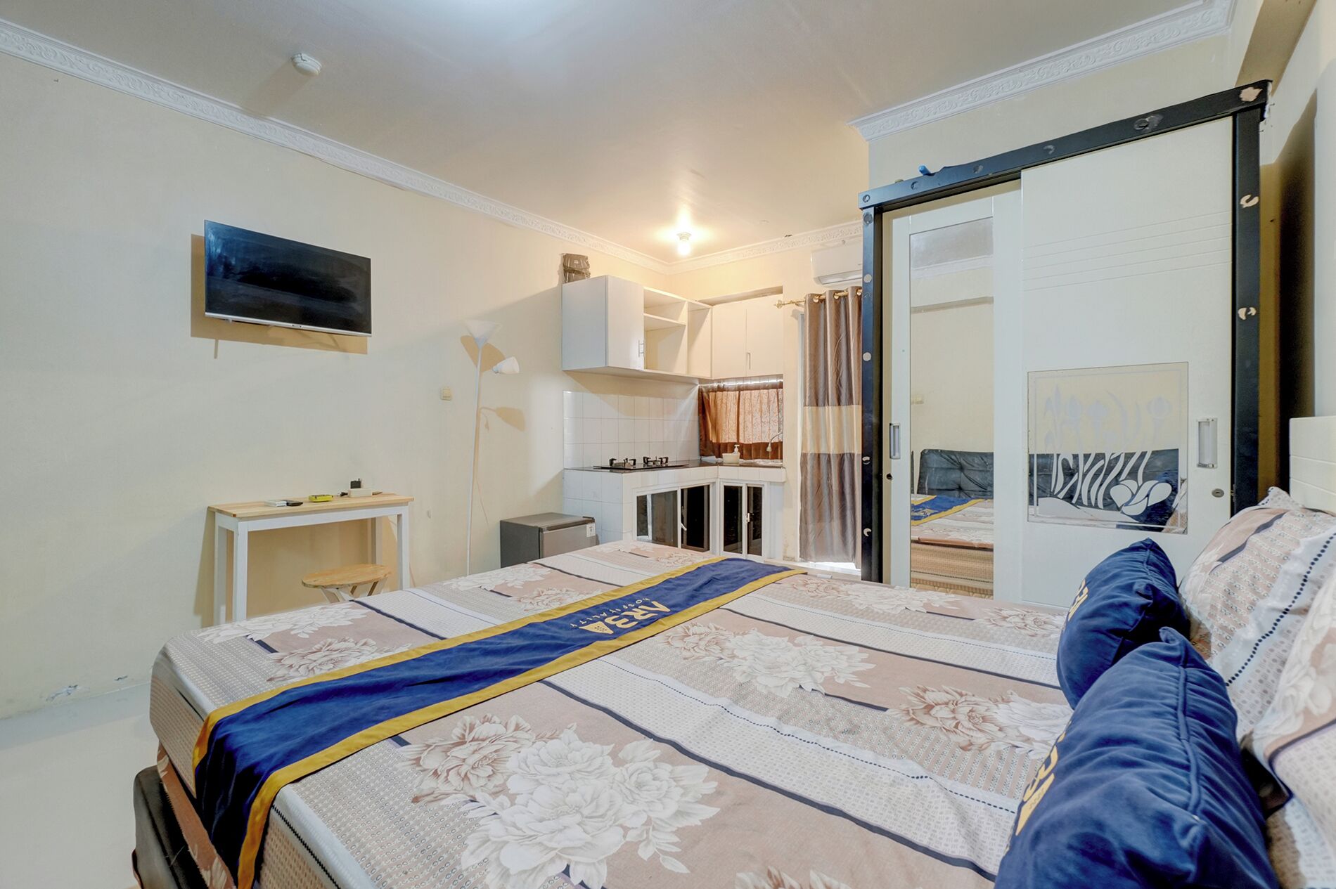 Une chambre à coucher comprenant un lit, un bureau, une armoire, un miroir et une salle de bain visible à travers une porte ouverte.