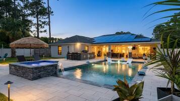 A backyard with a swimming pool, a hot tub, and a covered patio area.