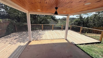 Una terrazza esterna coperta con tetto in legno, una ventola a soffitto nera e una ringhiera in metallo.
