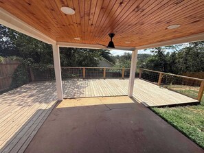 Een overdekt terras met een houten plafond, een zwarte plafondventilator en een metalen hekwerk.