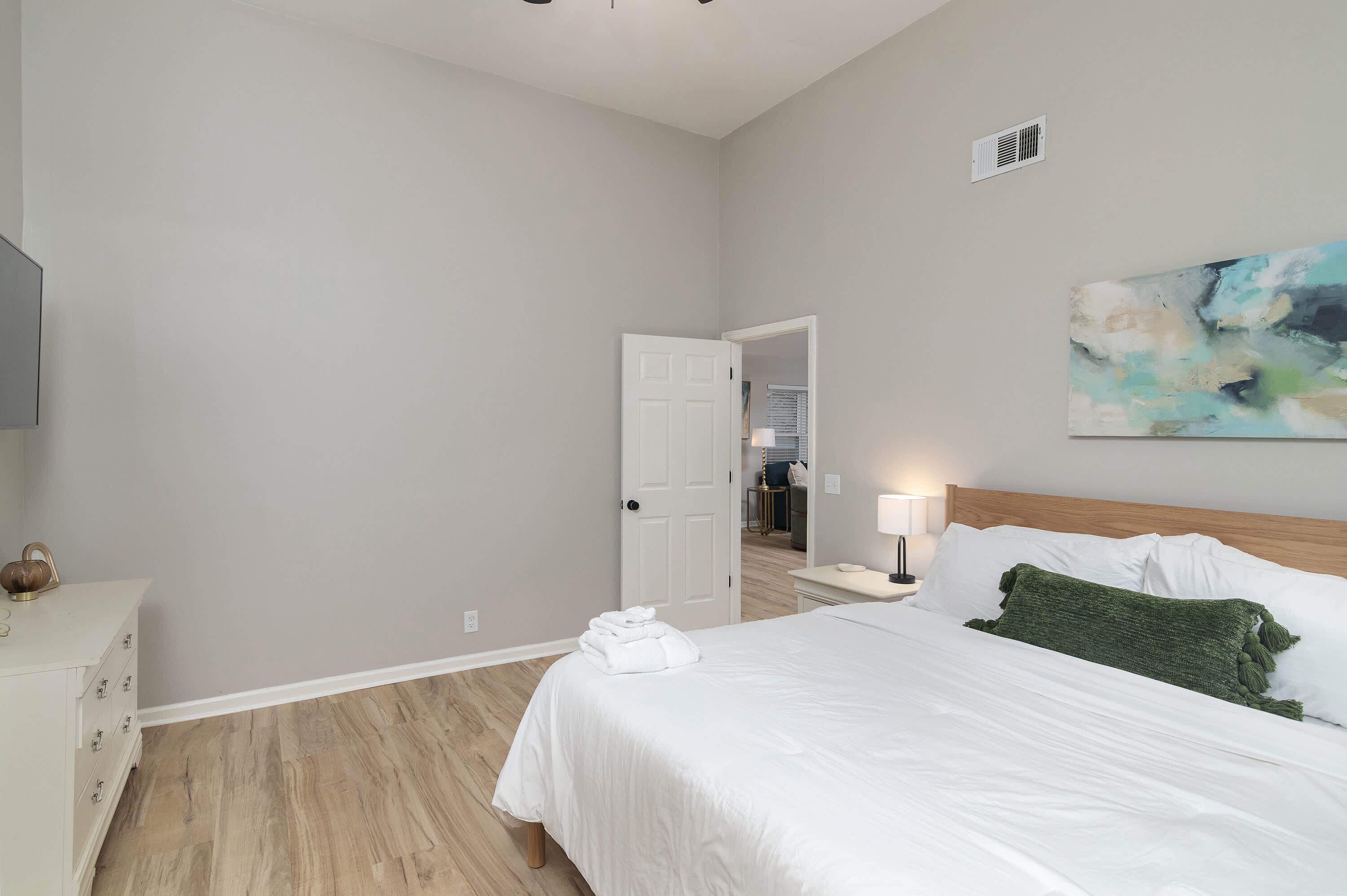 A hotel room with a bed, a bedside table, a lamp, and a painting on the wall.