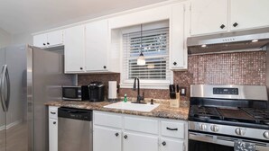 Uma cozinha moderna com eletrodomésticos de aço inoxidável, armários brancos e uma janela com persianas.