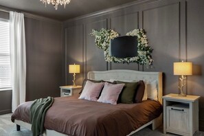 A bedroom with a large bed, two bedside tables, a wall-mounted TV, and a decorative floral arrangement. - The Everglow - Storybook Pool Home Near Disney (Davenport)