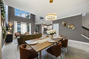 Een ruime eetruimte met een lange tafel, meerdere stoelen en een kroonluchter.