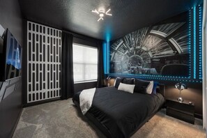 Een moderne slaapkamer met een groot bed, een plafondventilator, een wanddecoratie en een raam met jaloezieën.