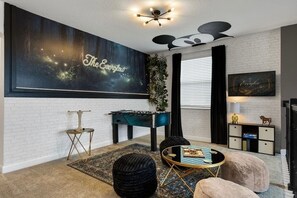 Uma sala de estar moderna com parede de tijolos brancos, uma grande pintura abstrata, mesa de pebolim, mesa de centro e sofá.