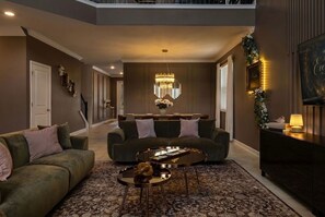 A spacious living room with a high ceiling, a chandelier, and a modern fireplace. - The Everglow - Storybook Pool Home Near Disney (Davenport)